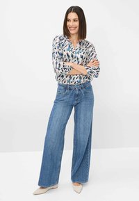 Long-sleeved, multicolored blouse with a pattern, paired with light blue wide-leg jeans and neutral-toned pointed toe shoes.
