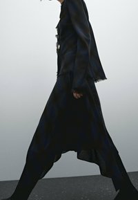 Ensemble noir comprenant une veste déchirée et une longue jupe, fabriqué à partir d'un tissu léger avec une silhouette fluide et des bords bruts.