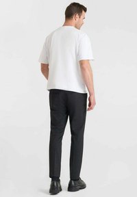 T-shirt bianca a maniche corte abbinata a pantaloni neri in tessuto testurizzato. I pantaloni hanno una vestibilità slim e sono indossati con scarpe nere.