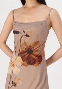 Robe sans manches marron avec un grand imprimé floral dans des teintes douces d'orange et de crème, dotée de délicates bretelles spaghetti et d'une texture lisse.