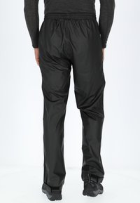Zwarte waterdichte broek met een elastische tailleband, een losse pasvorm en een gladde textuur. Voorzien van verstelbare enkelbanden voor een veilige pasvorm.