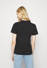 Must tänava must lühikeste varrukatega T-särk ümarate kaelustega, valmistatud pehmest puuvillast, sobilik disain, kantud heledate siniste teksadega.