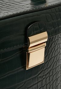 Sac en cuir noir texturé avec motif crocodile et une fermeture à loquet rectangulaire dorée brillante sur le rabat avant.