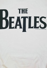 Felpa bianca con grande scritta nera che recita "THE BEATLES." Presenta una tasca frontale e un design semplice e casual.