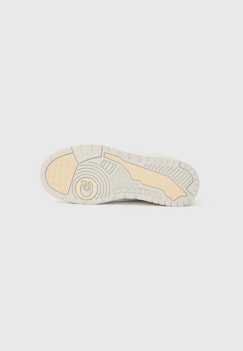 White sneaker outsole with textured patterns, featuring tan accents and brand logo. Durable rubber material designed for traction.