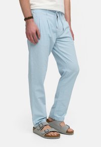 Helle blaue, strukturierte Hose mit einem Kordelzugbund, vorderen Falten und seitlichen Taschen, kombiniert mit grauen Sandalen mit doppelten Schnallen.