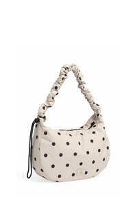 Beige håndtaske med prikker, der har en samlet stofskulderrem, blød tekstur, rund form og lynlås. Indeholder et logo-patch.