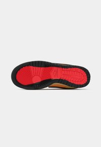 Semelle d'une basket Nike avec des motifs de bande de roulement rouges et noirs, montrant des rainures circulaires et linéaires pour l'adhérence.