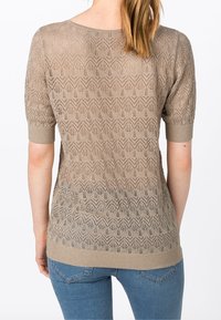 Top de punto beige con mangas cortas, que presenta un patrón zigzag texturizado y un dobladillo acanalado. Diseñado con un escote amplio y tejido abierto.