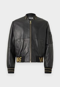 Μαύρο δερμάτινο bomber μπουφάν με χρυσές λεπτομέρειες, κλείσιμο με φερμουάρ, πλαϊνές τσέπες, ριμπ μανσέτες και ζώνη που φέρει το λογότυπο "VERSACE" σε χρυσά κεντήματα.