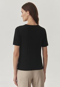 Maglietta nera a maniche corte con scollo rotondo, dal tessuto morbido e dalla vestibilità rilassata, abbinata a pantaloni a righe beige chiaro.