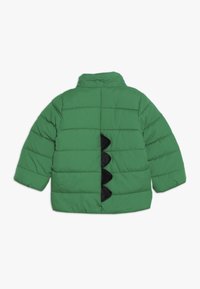Giacca verde gonfia con colletto alto, texture trapuntata e accenti neri a scaglie sul dorso. Presenta chiusure a scatto e maniche larghe.