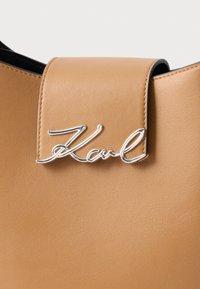 Pruuni naturaalsest nahast kott, millel on sile pind ja hõbedane logo "Karl" klapi kinnitusel. Lihtne, modernne disain.