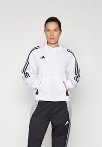 White hoodie with black three-stripe accents, kangaroo pocket, and hood. Paired with black joggers featuring a subtle logo and color-block design.