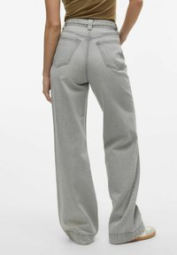 Los vaqueros gris de pierna ancha tienen una cintura alta, dos bolsillos traseros y un acabado limpio. La tela tiene una textura suave y un brillo ligero.