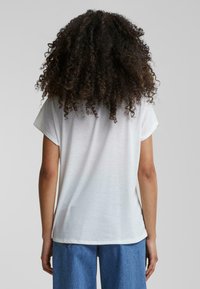 T-shirt blanc à manches courtes avec une coupe décontractée et un col rond, présentant une texture douce et des fentes sur les côtés, associé à un jean large bleu.