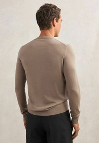 Jasnobrązowy sweter z długim rękawem i okrągłym dekoltem, miękka faktura, ściągacze na mankietach i u dołu. Noszony z ciemnymi spodniami, podkreślając dopasowaną sylwetkę.