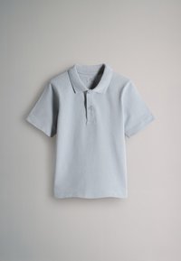 Polo bleu clair à manches courtes avec deux boutons sur fond beige, suspendu proprement avec un col et sans plis visibles.