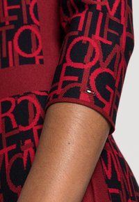 Stickad klänning med ett röd och marinblått grafiskt mönster, med en smal passform och texturerad tyg. Inkluderar en liten logotyp på ärmen.