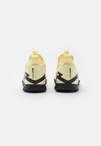 Yellow athletic shoes with black sole, featuring a sleek design, rear pull tabs, and a prominent black pattern on the sides.