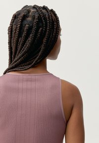 Ribbad linne i dammros med tunna axelremmar, som visar en figurnära design. Håret är stylat i intrikata flätade sektioner.