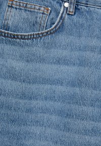 Tissu en denim bleu clair avec des coutures visibles, comportant une poche avant et une texture lisse. Décoloration subtile et design classique.