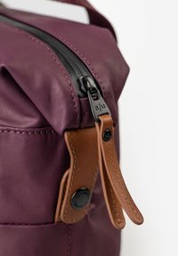 Close-up van een paarse stoffen tas met een dubbele bruine leren ritsen aan een zwarte rits schuiver.