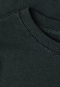 Gros plan d'un sweat-shirt vert foncé à col rond montrant la texture du tissu, les côtes au niveau de l'encolure et les coutures de l'emmanchure.