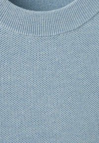 Jasnoniebieska dzianina o fakturowanej strukturze z prążkowanym, okrągłym kołnierzem. Powierzchnia ma równomierny, drobny wzór na całej powierzchni.