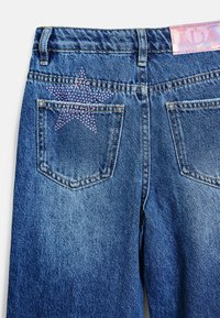 Jeans i denim har en blå tvätt med en texturerad yta. Bakhjulen är prydda med ett rosa strassstjärndesign.