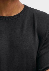 Suéter de punto negro con cuello redondo acanalado y mangas largas, con una textura suave y de color sólido en todo su diseño.