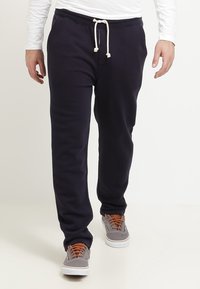 Marinblå mjukisbyxor i ett mjukt material, med ett elastiskt midjeband och vita dragsnören samt smalnande anklar. Kombinerat med grå sneakers.