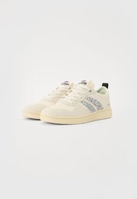 Baskets blanches et crème avec un corps beige texturé et un accent en imprimé léopard bleu. Comprend des lacets, un col rembourré et un onglet de talon noir.
