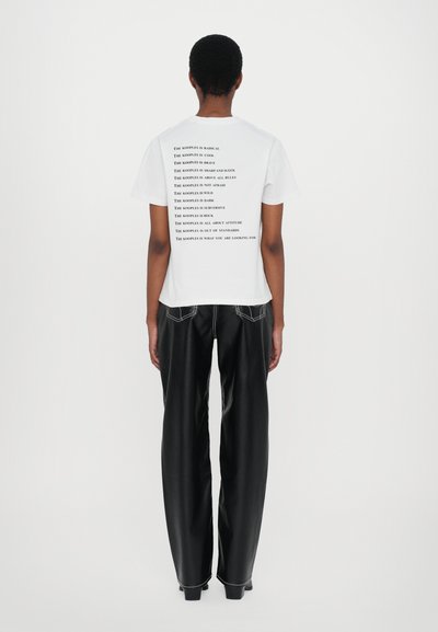 White T-shirt features black text printed on the back, paired with high-waisted black pants. The fabric has a smooth texture.