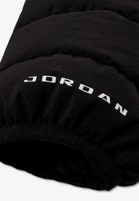 Черен подплатен наметал с бели букви "JORDAN", отпечатани върху материала, показващ еластичен детайл на ръба.