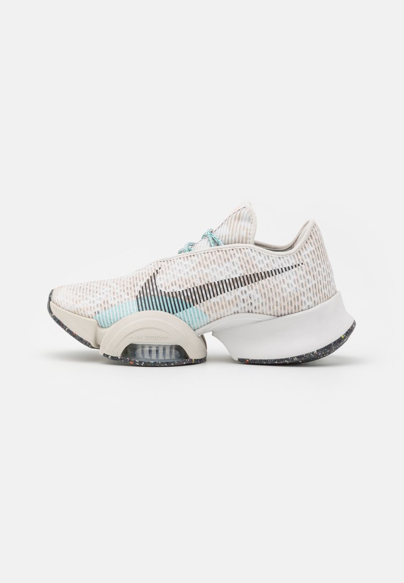 Sneakers bianchi con una tomaia in rete testurizzata che presenta accenti blu, uno swoosh nero e una suola curva unica con ammortizzazione visibile.