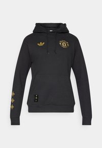 Μαύρο φούτερ με κουκούλα από βαμβάκι με εμπρόσθια τσέπη. Διαθέτει χρυσό λογότυπο της Manchester United, λογότυπο Adidas και χρυσές λεπτομέρειες στα μανίκια.