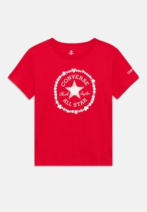 Camiseta de algodón roja con un diseño gráfico blanco que presenta una estrella central y texto circular que dice "Converse Chuck Taylor All Star."