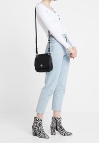 Black leather crossbody bag with a metallic logo, paired with blue high-waisted jeans and black and white zebra print ankle boots.