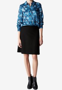 Blusa floreale blu con bottoni, abbinata a una gonna nera. Calzature: stivaletti neri alla caviglia. Tessuto morbido e design strutturato.