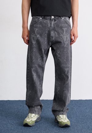 Jeans in denim grigio scuro con un motivo testurizzato, vestibilità ampia, cinque tasche e dettagli ricamati, abbinati a sneakers con dettagli verde.