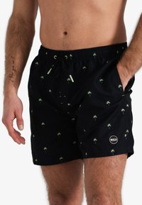 Zwarte zwembroek met groen palmenpatroon, elastische tailleband met trekkoord, en zijzakken. Bevat een logo-opdruk op de zoom.