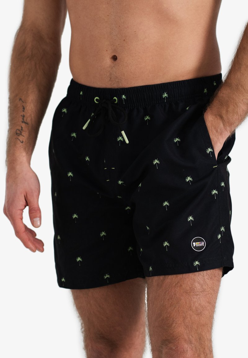 Zwarte zwembroek met groen palmenpatroon, elastische tailleband met trekkoord, en zijzakken. Bevat een logo-opdruk op de zoom.