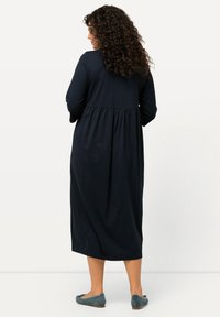 Granatowa, długa sukienka z długimi rękawami, zebranym pasem, zwiewnym fasonem i miękką, teksturowaną tkaniną. Noszona z zielonymi balerinkami.