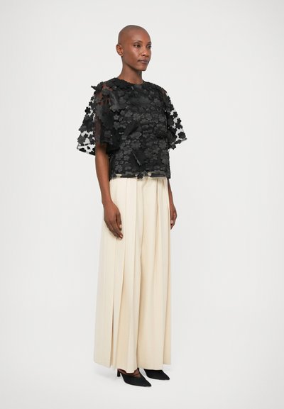Sort blomstret blonde top med korte, lagdelte ærmer, parret med cremefarvede højtaljede, plisserede bukser og sorte spidse hæle.