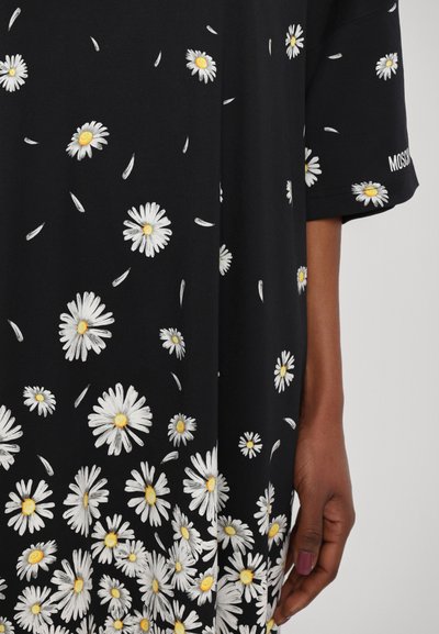 Sort stof t-shirt med hvid marguerit broderi med gule center. Korte ærmer med logo-accente på ærmekanten.