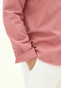 Ljust rosa skjorta tillverkad av ett mjukt tyg, med knäppning vid ärmslutet och en avslappnad passform. Matchad med vita byxor som har en sidoficka.