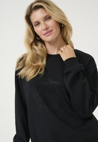 Zwarte sweatshirt met een ronde halslijn, voorzien van een textuurontwerp van rhinestones aan de voorkant en lange mouwen. Zachte stoftextuur.