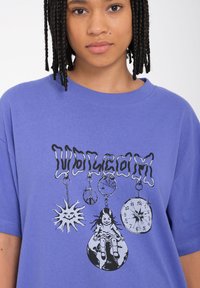 Camiseta de algodón morada con un ajuste holgado que presenta un estampado gráfico de un sol, un signo de paz y un reloj. Ilustraciones en blanco y negro en la parte delantera.