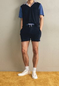 Shorts bleu marine et un polo bicolore bleu avec un col gris. Associé à des baskets blanches et des chaussettes jusqu'aux chevilles. Tissu doux et décontracté.